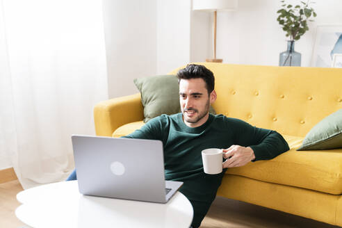 Mann mit Laptop und Kaffee auf gelbem Sofa. - ISF26560