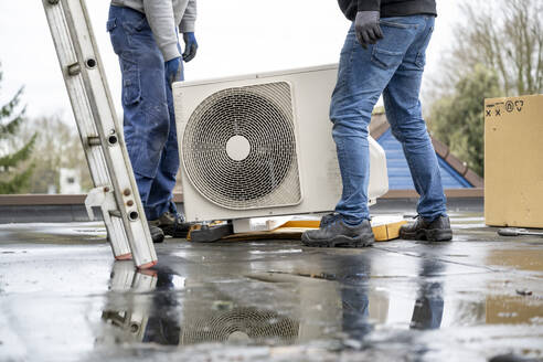 Zwei Arbeiter, die an einem bewölkten Tag eine Klimaanlage auf einem Dach installieren. - ISF26586