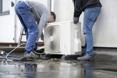 Zwei Techniker bei der Installation eines Außengeräts einer Wärmepumpe auf einem Dach. - ISF26588
