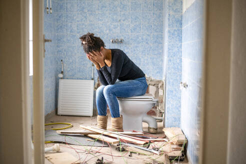 Erschöpfter Hausbesitzer sitzt auf einer Toilette in einem unfertigen Badezimmer - ISF26719