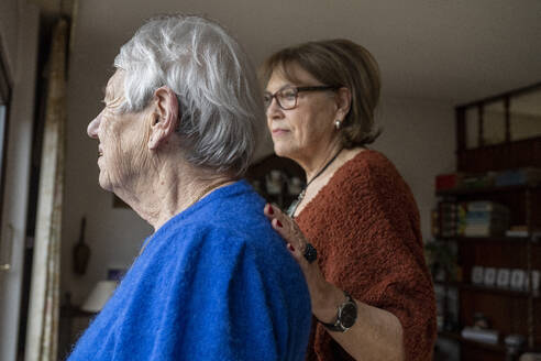 Two elderly friends standing looking out of the window consoling one another - ISF26831