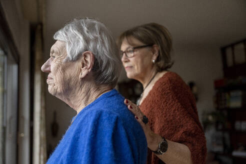 Two elderly friends standing looking out of the window consoling one another - ISF26832