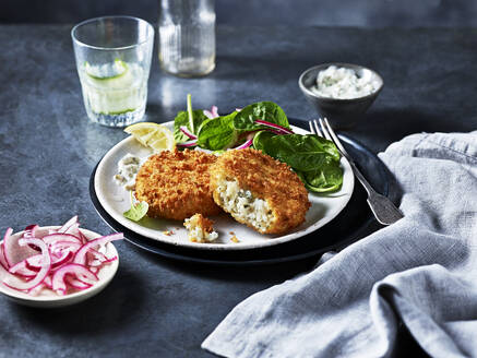 Crispy breaded fish with a side of fresh spinach salad and sliced pickled onions on a dark, elegant table setting. - ISF26995