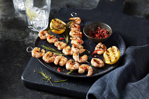 Grilled shrimp skewers with lemon and dipping sauce on a dark, rustic table setting. - ISF27010