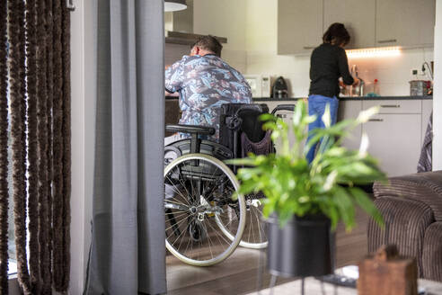 Eine Frau bereitet das Mittagessen für ihren Mann vor, der in seinem Rollstuhl am Tisch sitzt - ISF27120