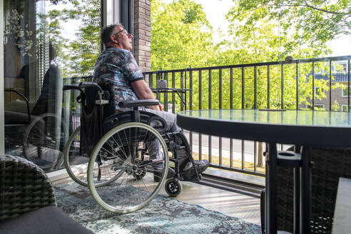Ein Mann im Rollstuhl denkt über das Leben nach, während er auf seinem Balkon sitzt und sich entspannt und die Aussicht genießt - ISF27121