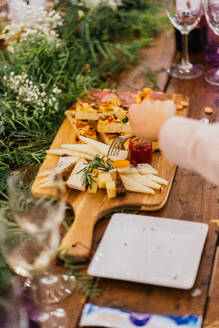 Anonymous guest reaches for a selection from a bountiful cheese platter amidst a floral banquet, with glasses of wine and cheerful ambiance - ADSF55268