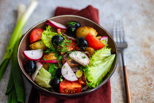 Close-up of a hearty bowl of Mediterranean salad, garnished with dill, featuring roasted potatoes, olives, cherry tomatoes, spring onions, crisp lettuce, and fresh radishes - ADSF55295