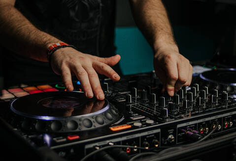 A DJ mixes tracks with skilled hands on a professional console, creating energetic beats at a club or event - ADSF55326