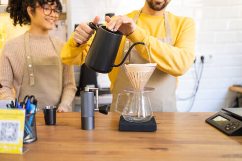 Barista carefully pours hot water into a coffee dripper over a carafe in a cozy cafe setting. - ADSF55468