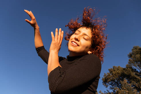 A joyful contemporary dancer moves gracefully under a clear blue sky, her red curls bouncing in the sunlight - ADSF55502