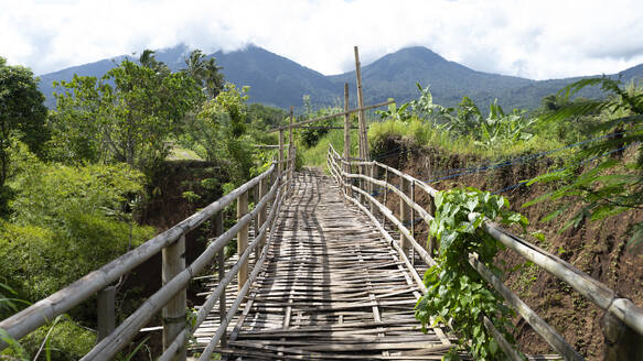 Rustic bamboo bridge crossing a lush ravine with Mount Agung shrouded in clouds in the background, Bali - ADSF55554