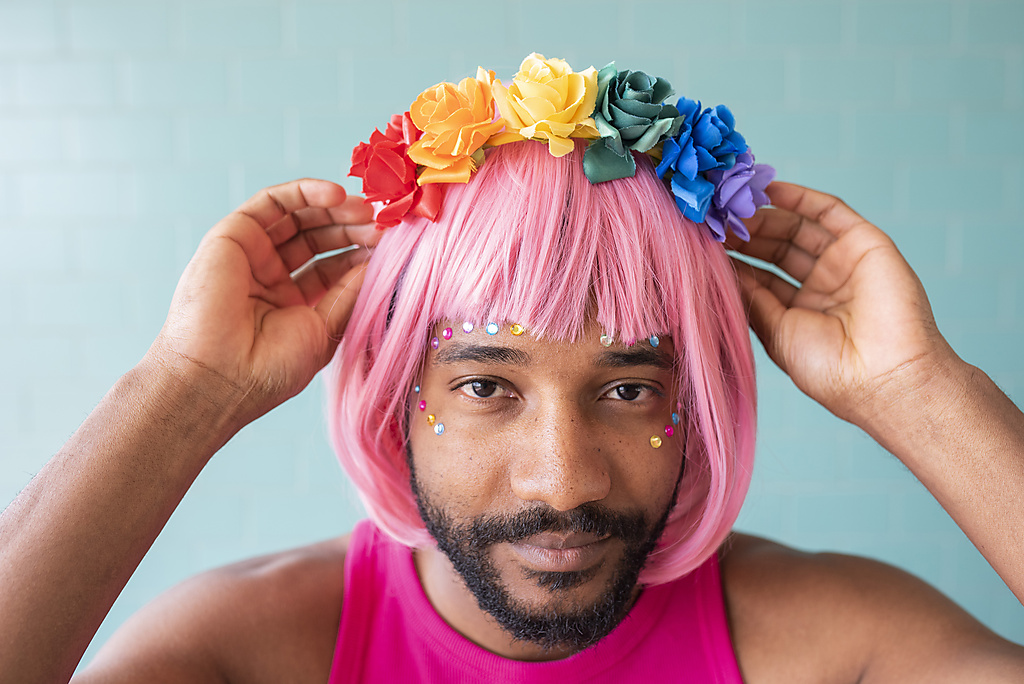 Junger homosexueller Mann, der sein Blumen-Diadem vor einer Wand zurechtrückt